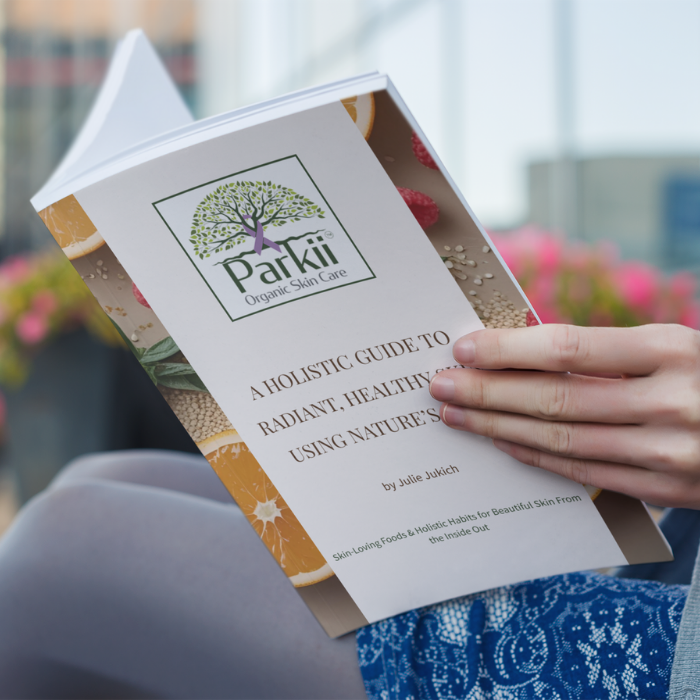 Person reading a Parkii Organic Skin Care booklet titled "A Holistic Guide to Radiant, Healthy Skin Using Nature's Best," with a tree logo and decorative botanical border.