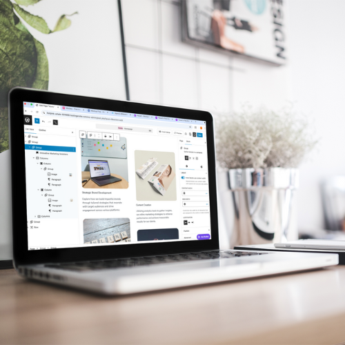Laptop on a desk displaying a digital brand strategy layout, with papers and a potted plant beside it.